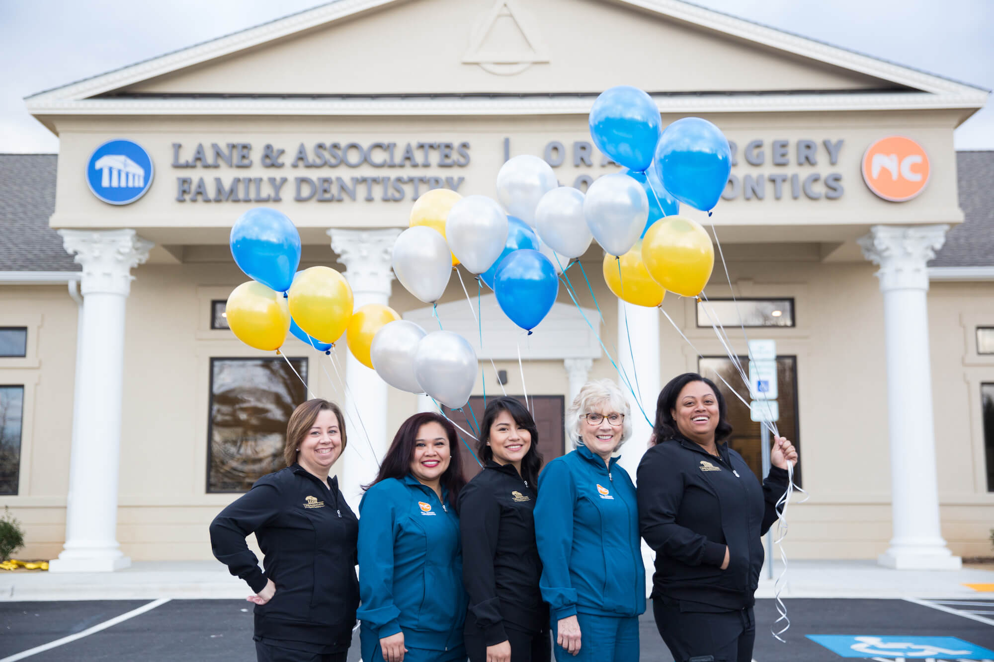 Dental employees outside of the office holding blue and gold balloons smiling