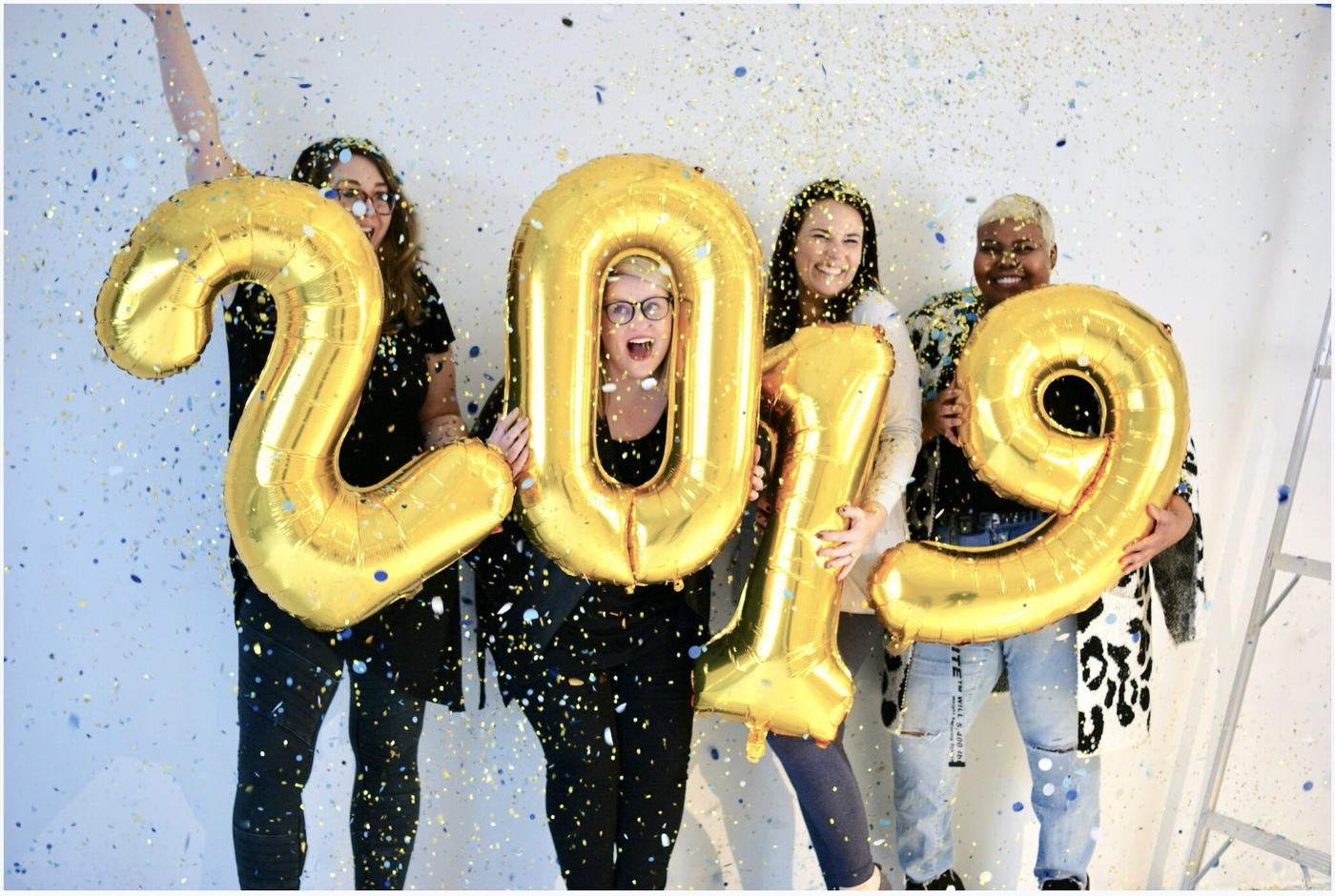 Gold 2019 number balloons being held by 4 people with confetti falling