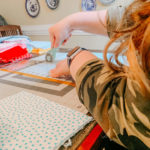 girl cutting out cotton pieces of fabric for face masks