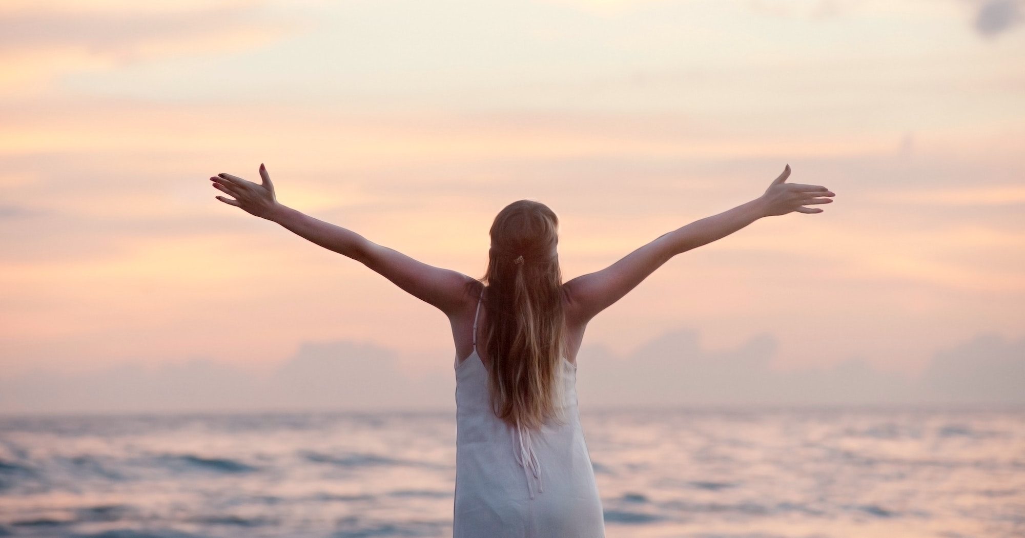 girl raising arms to the sky at sunset beach