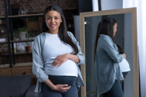 african american pregnant woman with big belly standing at mirror